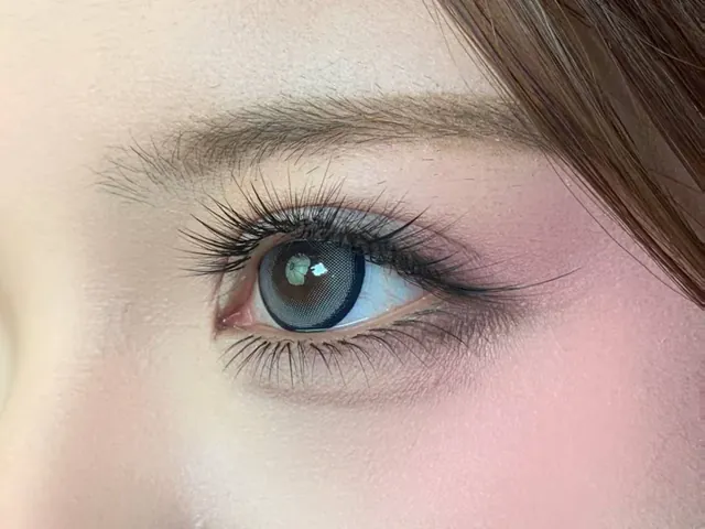 Close-up of an eye with a wispy lash extension set, a blue-grey contact lens and rose blush