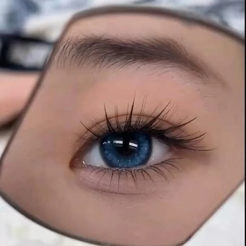 Close-up of an eye with fresh lash extensions, reflected in a hand mirror — yeux by qun