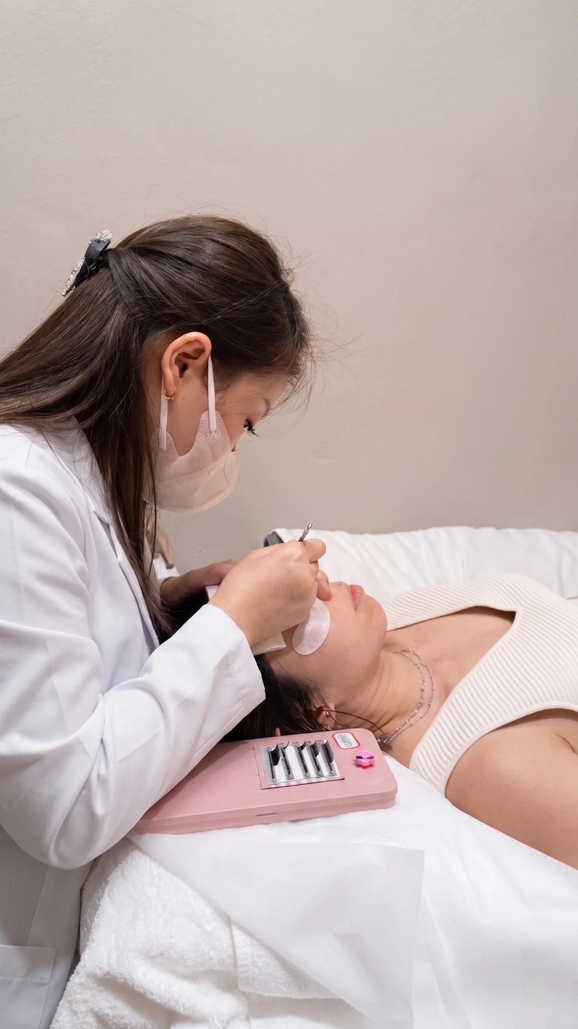 Qun applying lash extensions on a client at the yeux by qun Hougang studio — focused, masked, working in profile